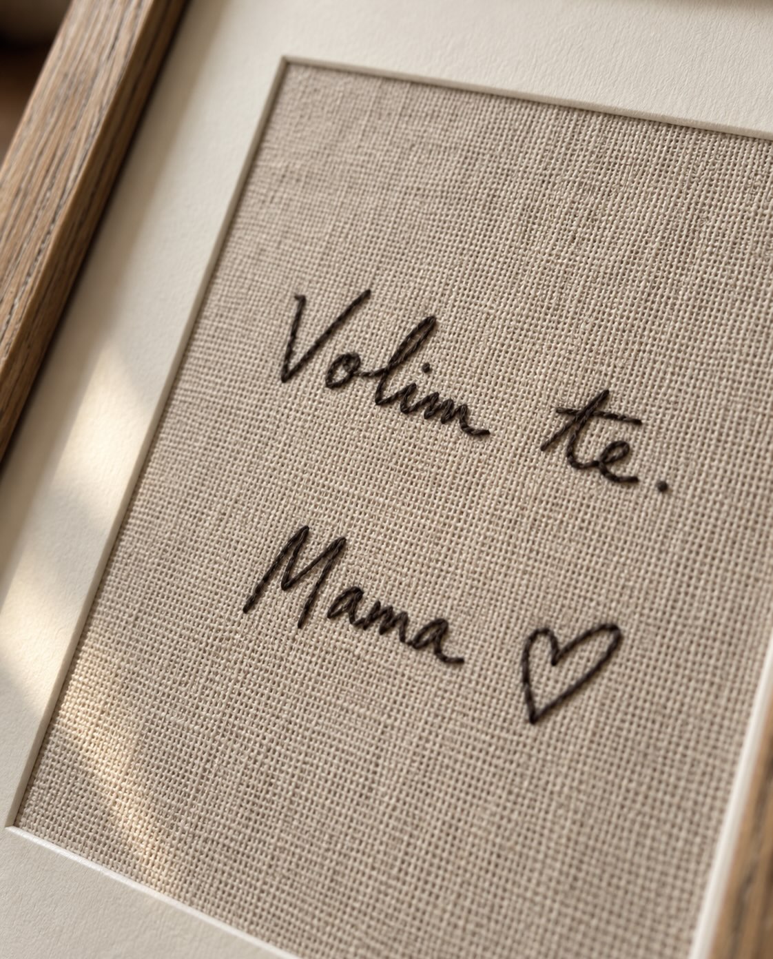 Detalj vezenog rukopisa ‘Volim te, Mama’ na tkanini u drvenom ramu